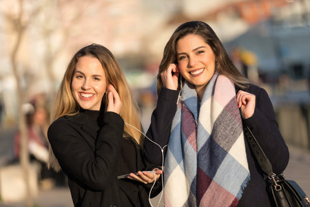 Young pretty girls best friends smiling and having fun, walking at the city. Shopping. Wearing stylish outerwear. Bright make up. Positive emotions. Outdoors lifestyle fashion close up portraitの写真素材