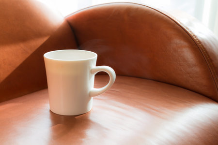 white cup of hot tea on brown leather chairの写真素材