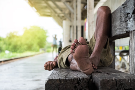 closeup homeless man's feet sleeping on wood bench at train stationの写真素材