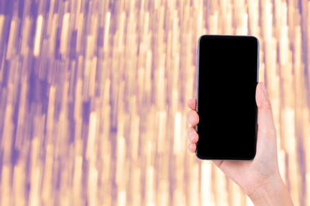 woman hand holding mobile phone on bright shiny bokeh backgroundの写真素材