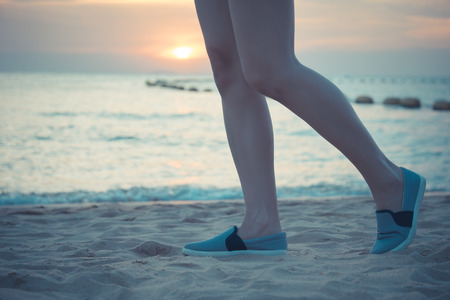 part of woman legs walking on the beach while sunsetの写真素材