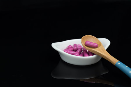 pink capsules in white bowl with spoon on black background