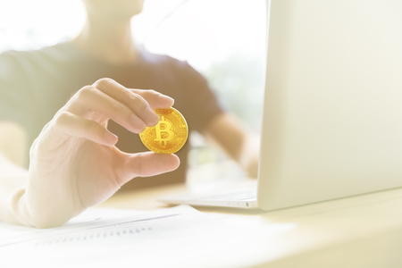 man holding golden bitcoin while working with laptop and documentsの写真素材