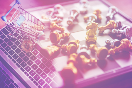 chessman on board game with golden bitcoin in shopping cart on laptop, business and finance conceptの写真素材