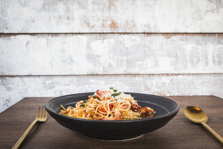 stir fried spaghetti with bacon, chili, and garlic on black dish served on wood tableの写真素材
