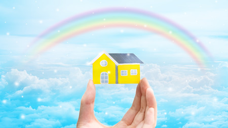 home shape wood model on hand with rainbow sky backgroundの写真素材