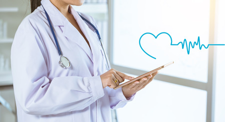 part of female doctor holding tablet with heart cardiogram icon, health conceptの写真素材