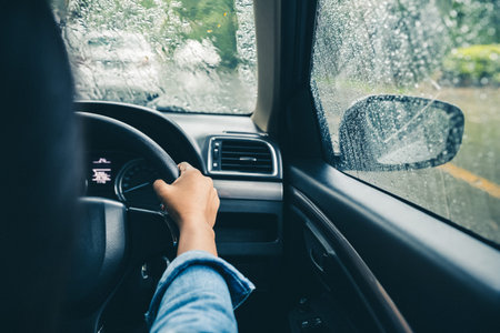closeup driver's hands on steering wheel driving on rainy day
