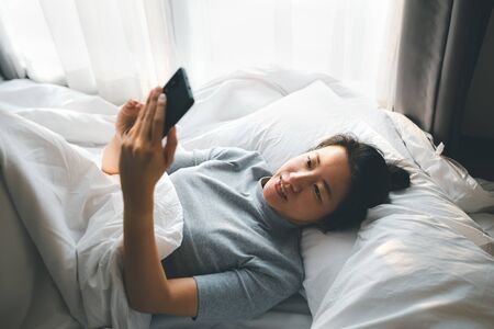 woman lying on bed using smartphone, lifestyle conceptの写真素材