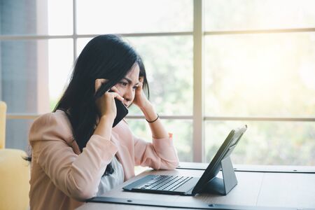 beautiful working woman using smart phone with tablet on desk with moody emotionalの写真素材