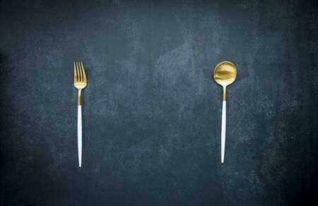 golden spoon and fork on dark blue background with copy space, food and drink, dining conceptの写真素材