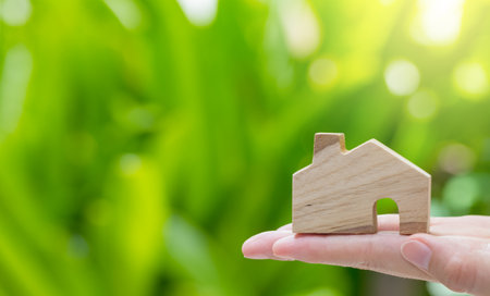 wooden home model on woman hand with green nature background on sunny dayの写真素材