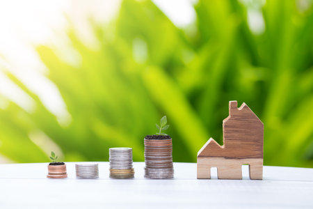 coin stacks arrangement and wooden home model with green nature background, money saving conceptの写真素材
