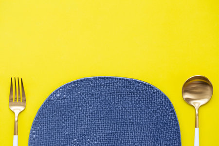 blank blue rough ceramic dish with brass spoon and fork on yellow background, food and drink, dining...