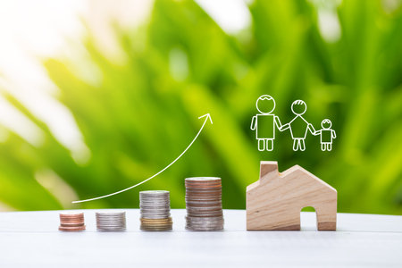 coin stacks arrangement and wooden home model with graphic of family on green nature background,...