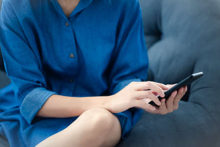 closeup woman with casual dress using mobile phone on sofa, work from home conceptの写真素材