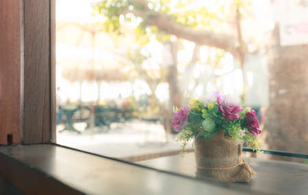 rose flowers in sacking bag pot outside window with blurred big tree backgroundの写真素材