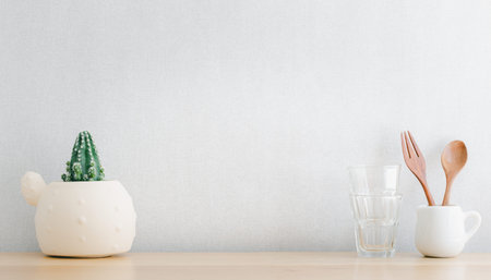 kitchenware and utensils and cactus decorated on wooden shelf or counter with light gray wall...