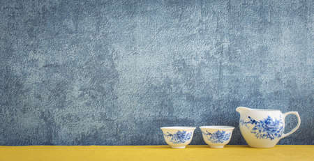 classic ceramic jar and glasses decorated on yellow shelf or counter with blue wall background and copy space, home decorの写真素材