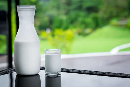 bottle of milk and glass on table with green nature backgroundの写真素材