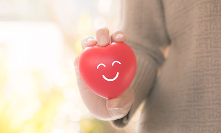 closeup woman hand holding red heart with smiling emoticon, healthcare conceptの写真素材