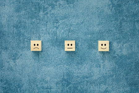 different emotion faces on wooden cube with blue background for satisfaction survey, mental health...