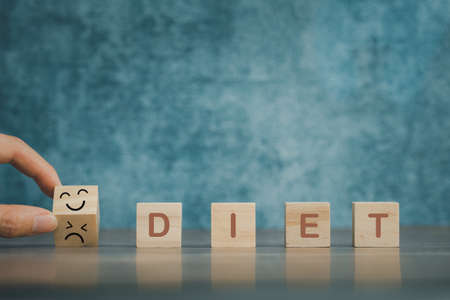 hand deciding to diet or not, diet word on wooden cube with blue background, healthy conceptの写真素材