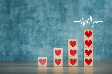 heart on wooden cubes arranged in bar graph shape with cardiogram on blue background, health conceptの写真素材