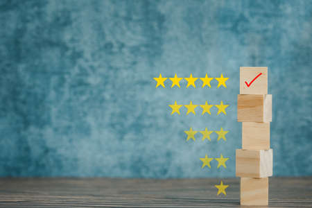 check mark on wooden cube with star rating on blue background, satisfactory survey conceptの写真素材