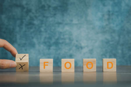 hand deciding yes or no for food concept, food word on wooden cube with blue backgroundの写真素材