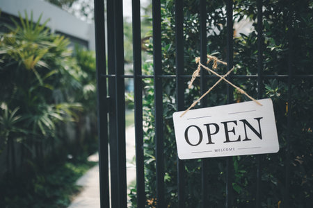 Open sign hanging in front of cafe gate with green garden background