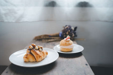 macadamia croissant and strawberry cream puff on wood table with transparent curtain background, bakery and cafeの写真素材