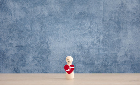 wooden doll hug red heart on blue background, love and healthcare conceptの写真素材