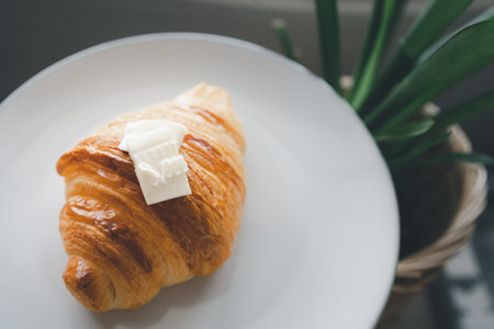 closeup plain croissant topped with piece of butter in white dishの写真素材