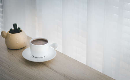 cup of hot cocoa with cactus pot on wood table besides window, refresh and relax conceptの写真素材