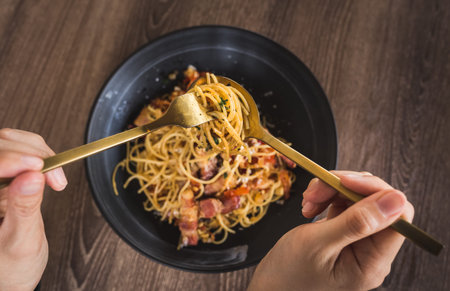 shot of person's hand having spicy bacon pasta on tableの写真素材