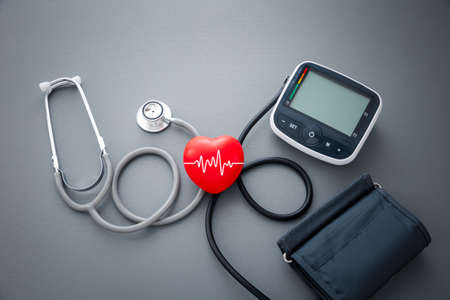 red rubber heart and stethoscope with blood pressure measurement machine on dark grey background, health conceptの写真素材