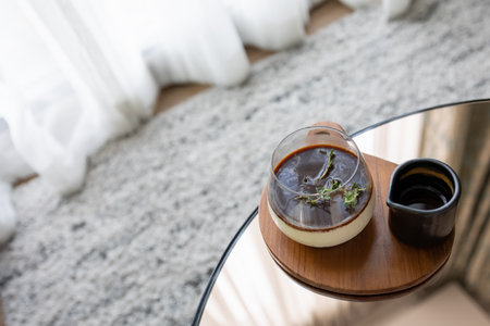 top view glass of coconut pudding topped with hot coffee on table besides windowの写真素材