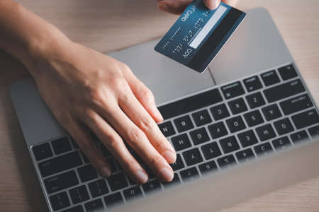 closeup woman hand holding credit card on hand and typing code on laptop, online payment conceptの写真素材