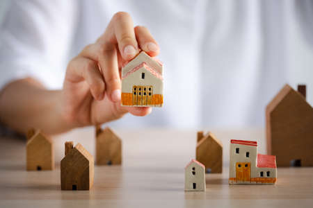 closeup woman hand holding beautiful home model with many wood homes on table, investment conceptの写真素材