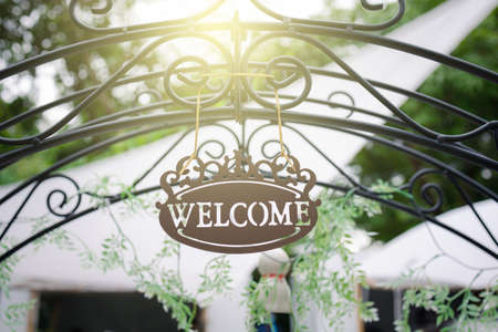 vintage welcome sign hanging on arched entrance in garden with sun lightの写真素材