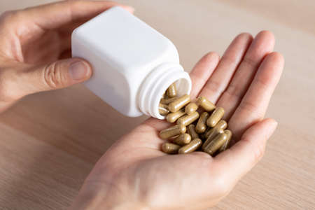 closeup woman pouring herb capsules from bottle to another hand, healthcare and medical conceptの写真素材