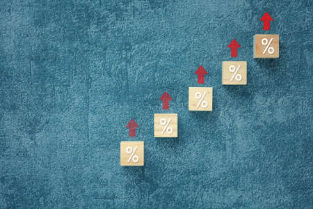 wooden cubes with percentage sign and up arrow on blue background presented for interest rate growing, business inflation conceptの写真素材