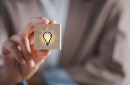 closeup hand holding wood cube block with light bulb icon, thinking and idea conceptの写真素材