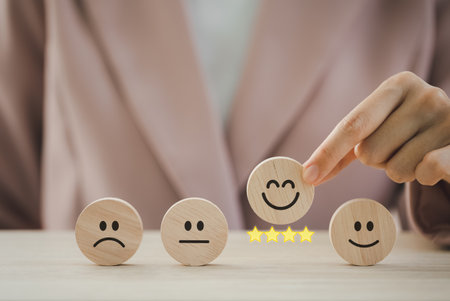 closeup businesswoman hand picking happy emotion face on wooden round piece arranged on table for satisfaction survey, mental health assessmentの写真素材