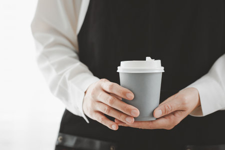 closeup woman wearing apron holding paper cup of hot coffeeの写真素材