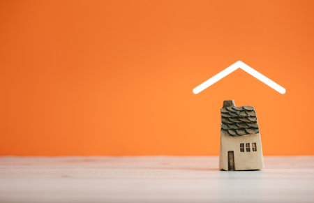 isolated ceramic home model covered by roof icon on orange background with copy space on leftの写真素材
