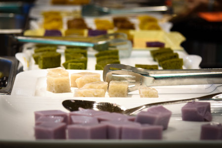 A variety of pastry delicacies in the buffet restaurant. Colorful cubed desserts on plates, with tongs and spoons beside.の写真素材