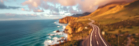 Coastal road winding along cliffs under a colorful sky during sunset near a serene oceanの素材