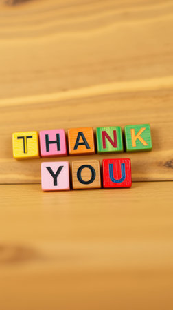 Colorful blocks arranged to spell words of appreciation on a wooden surface in a cozy settingの素材
